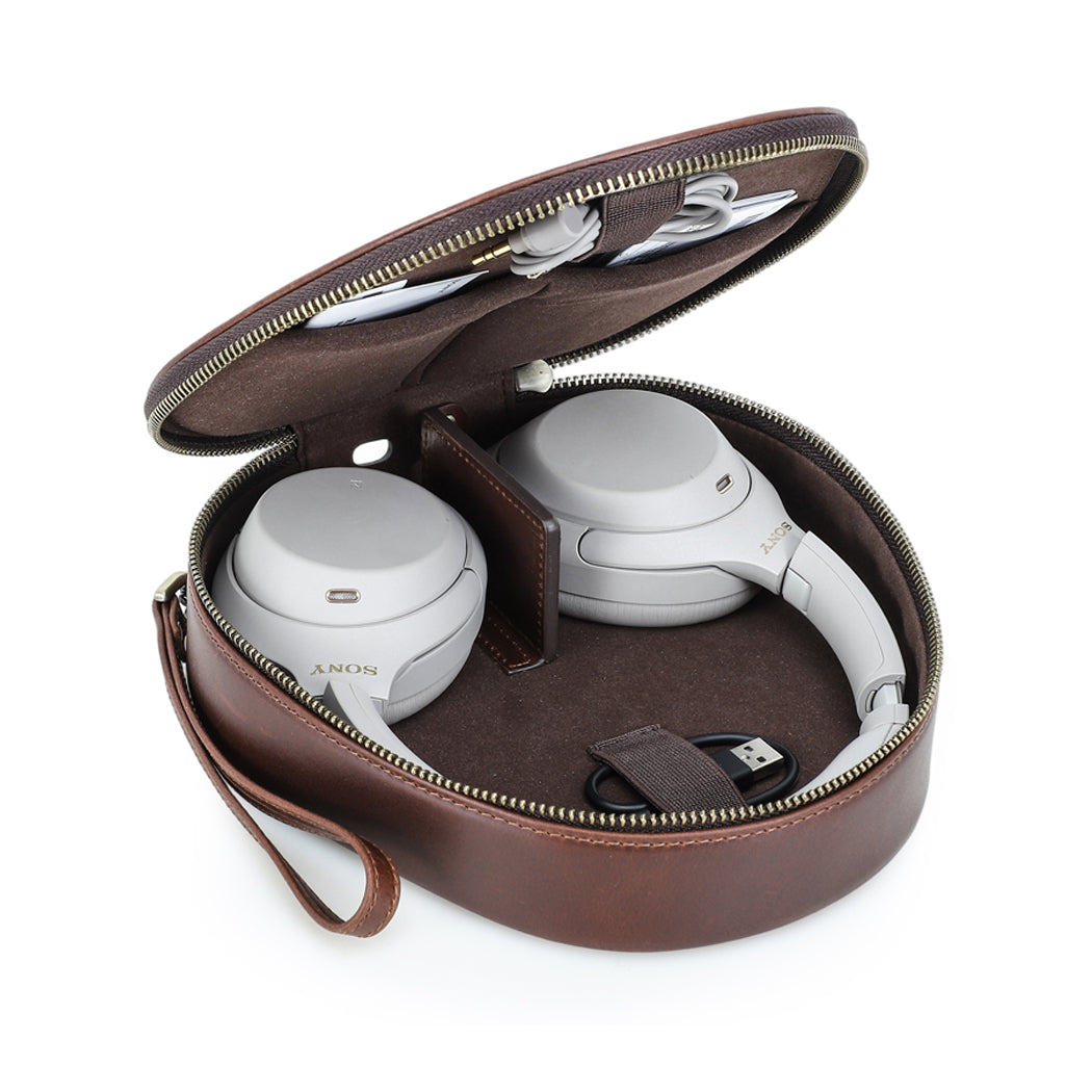 White Sony WH-1000XM5 headphones in a half-open brown headphone case with a black USB cable, and coiled auxiliary cable, organized neatly for travel