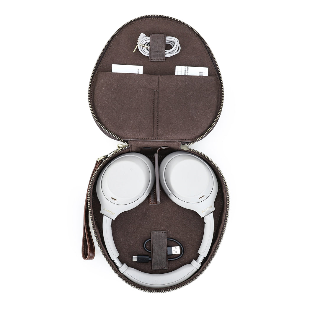 Open brown headphone case containing white over-ear headphones, a black USB cable, and coiled auxiliary cable, organized neatly for travel