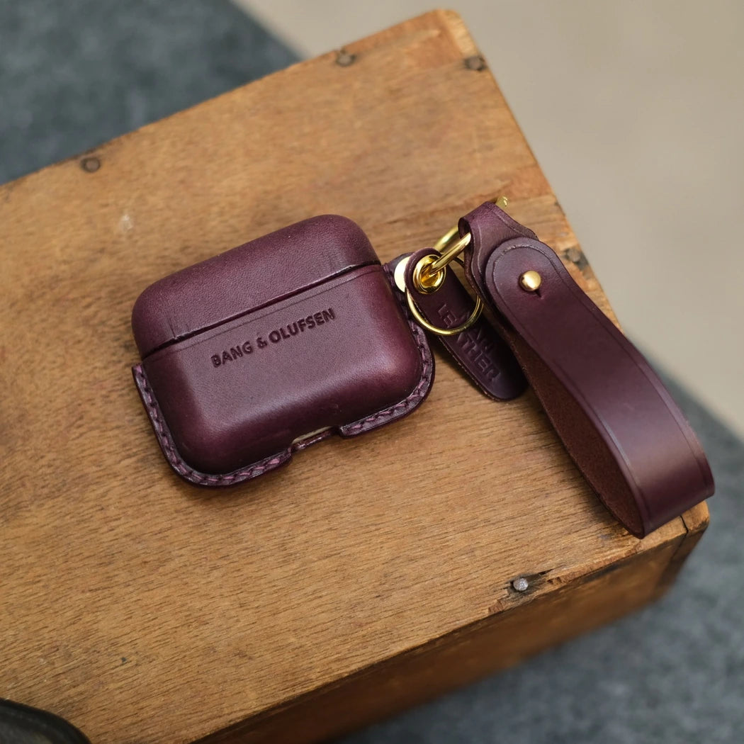 Dark purple handcrafted leather earbuds case cover for Bang & Olufsen Beo Grace with matching leather keychain strap, featuring debossed BANG & OLUFSEN logo.