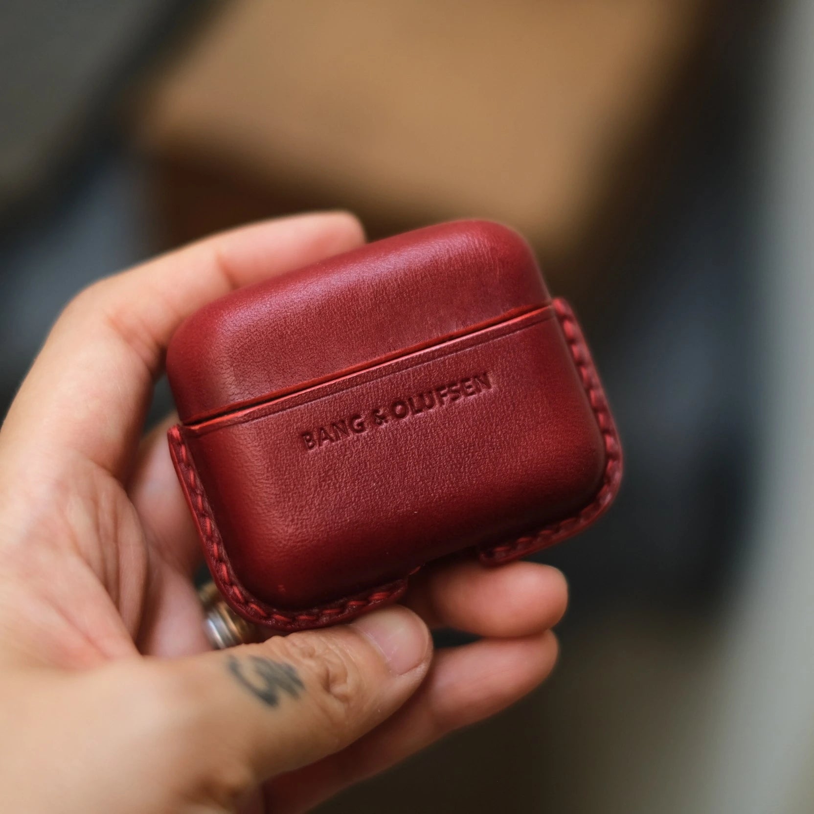 Hand holding a wine red handcrafted leather protective case for Bang & Olufsen Beo Grace case, featuring debossed BANG & OLUFSEN logo.