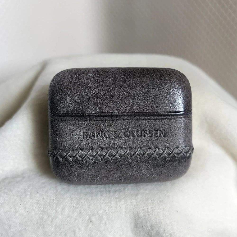 Premium Dark Grey leather earbuds cover for B&O Beo Grace with a vintage marbled finish and artisanal cross-stitch, showcased on a light fabric background.