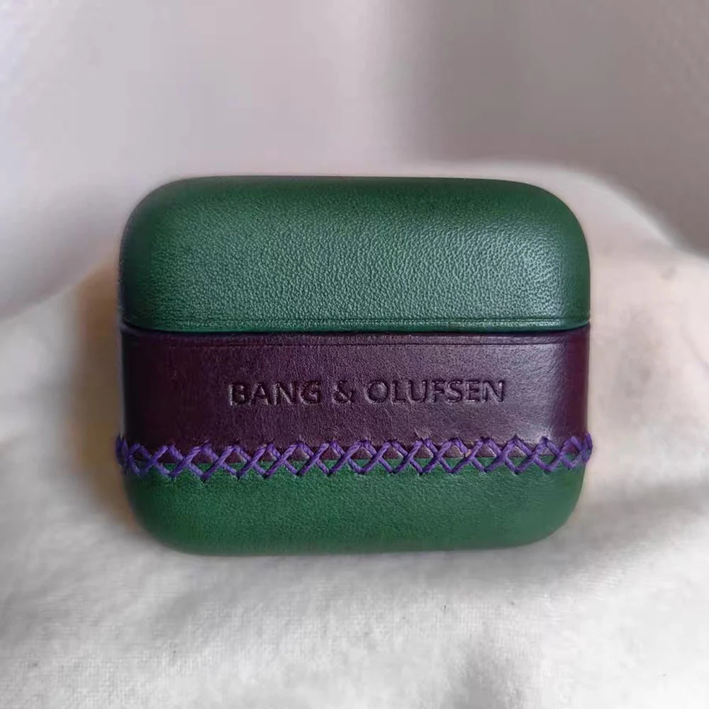 Vista frontal de la funda de cuero de plena flor verde y morada hecha a mano por Ronuo para los auriculares Bang & Olufsen Beo Grace, con una banda con logo en relieve hundido y costura artesanal en punto de cruz morada