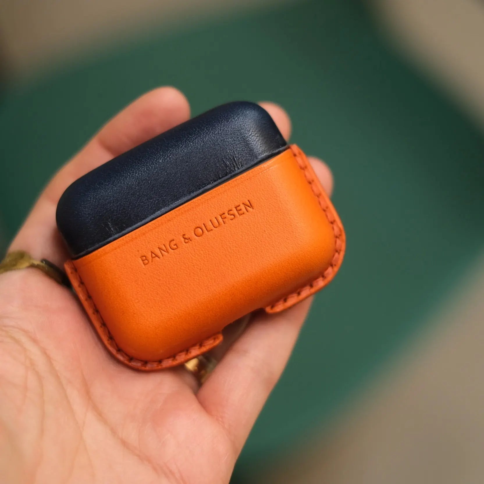 Hand holding a navy blue and orange two-tone handcrafted leather protective case for Bang & Olufsen Beo Grace, featuring debossed BANG & OLUFSEN logo.
