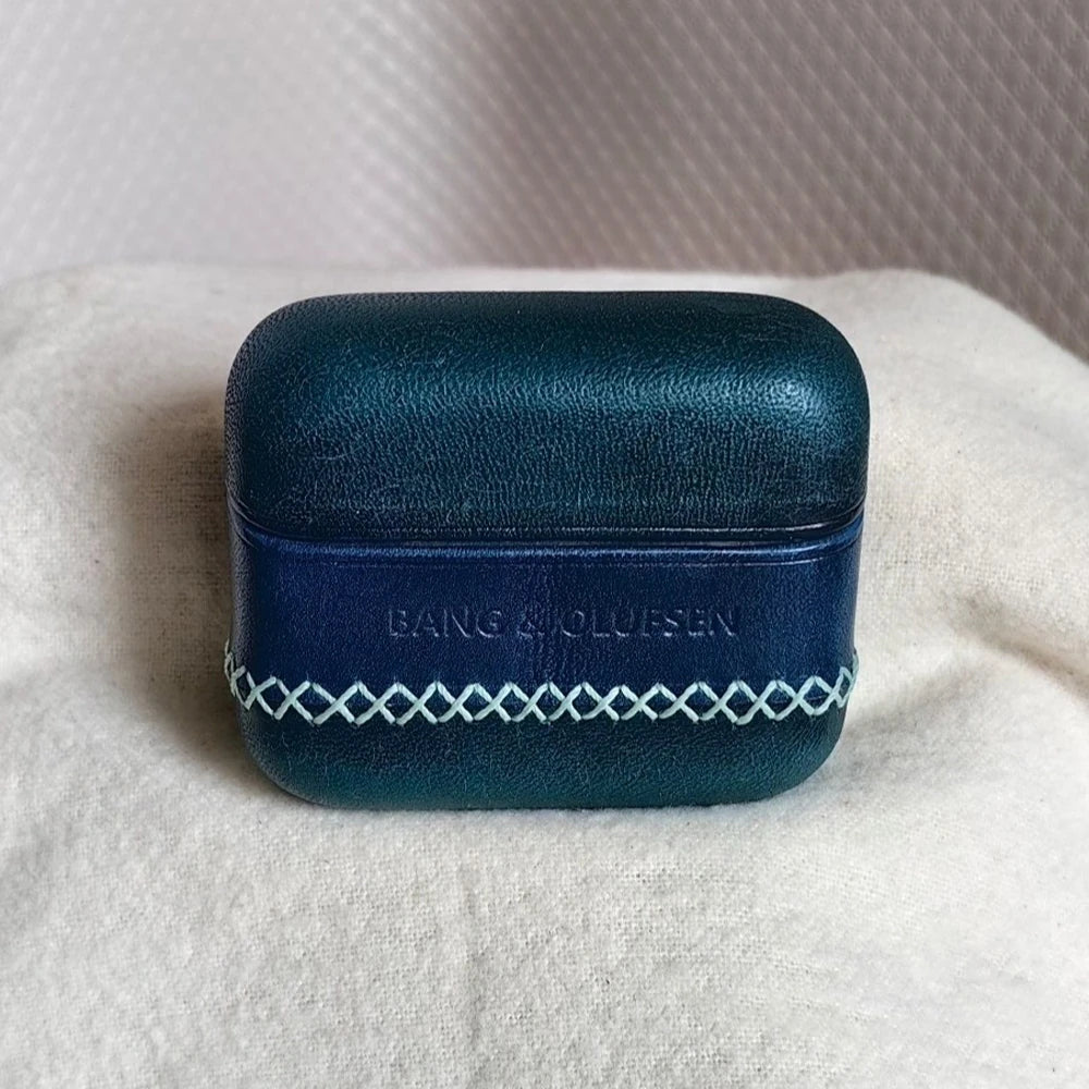 Detailed shot of the Peacock Blue leather earbuds cover for B&O Beo Grace, featuring a navy blue central band and striking white artisan cross-stitching for a modern look.