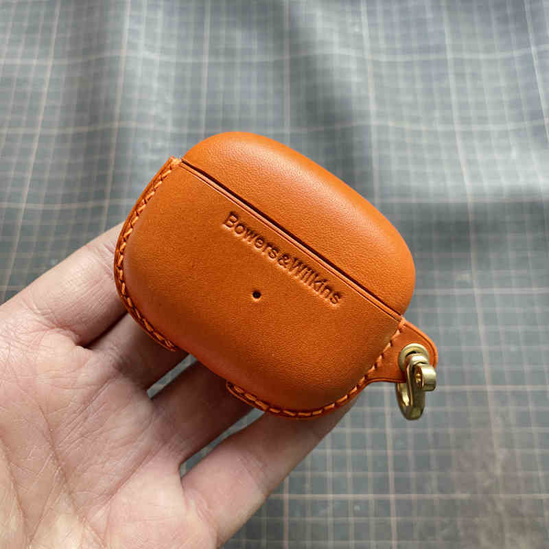 Schutzhülle aus echtem Leder für Bowers & Wilkins Pi8 Pi6 - Nahaufnahme einer Hand, die eine orangefarbene Hülle mit Metallverschluss hält.