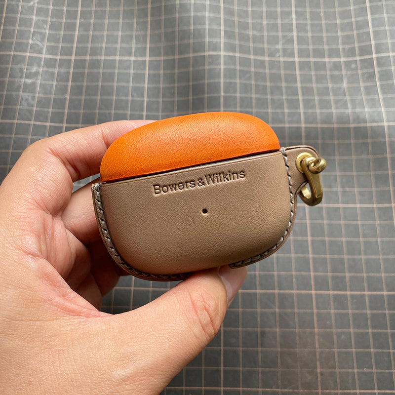 Genuine leather protective case for Bowers &amp; Wilkins Pi8 Pi6 bluetooth earbuds — close-up of a hand holding orange (top) and elephant grey (bottom) case with metal clasp