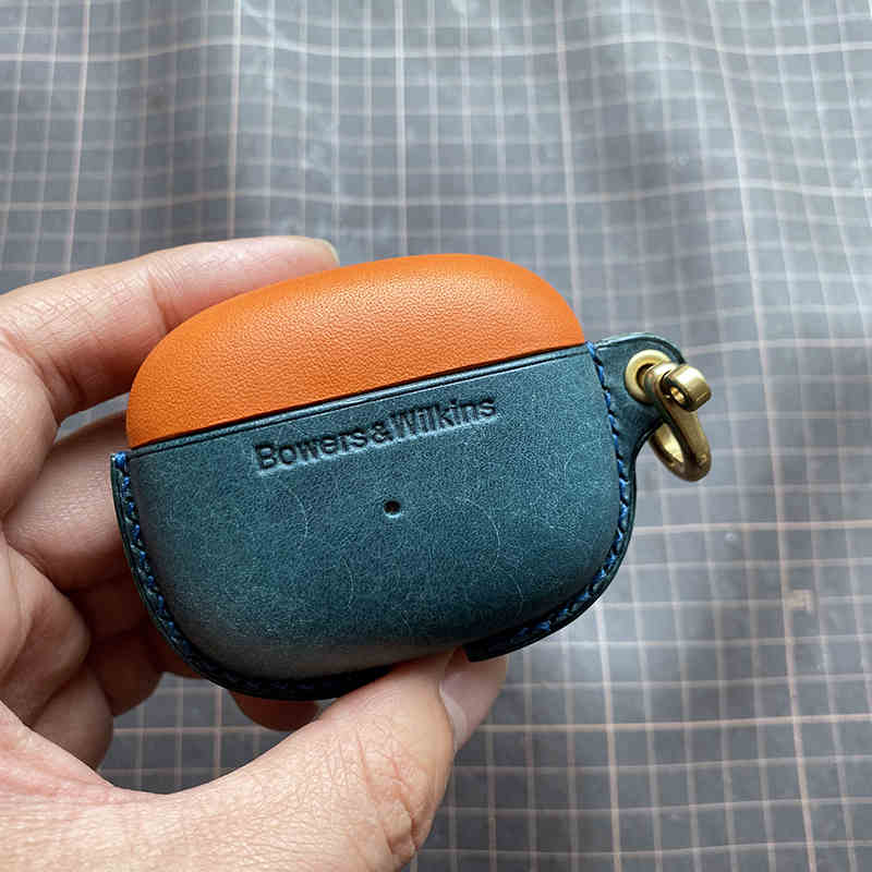 Schutzhülle aus echtem Leder für Bowers & Wilkins Pi8 Pi6 - Nahaufnahme einer Hand, die eine orangefarbene (oben) und eine pfauenblaue (unten) Hülle mit Metallverschluss hält.