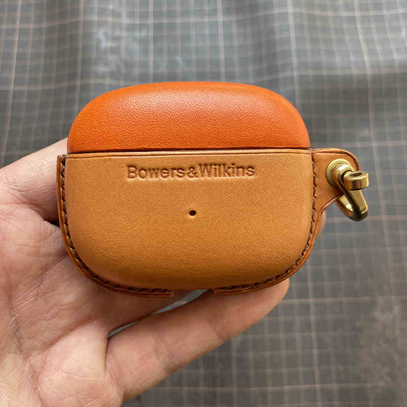 Schutzhülle aus echtem Leder für Bowers & Wilkins Pi8 Pi6 - Nahaufnahme einer Hand, die eine orangefarbene (oben) und eine gelbbraune (unten) Hülle mit Metallverschluss hält.