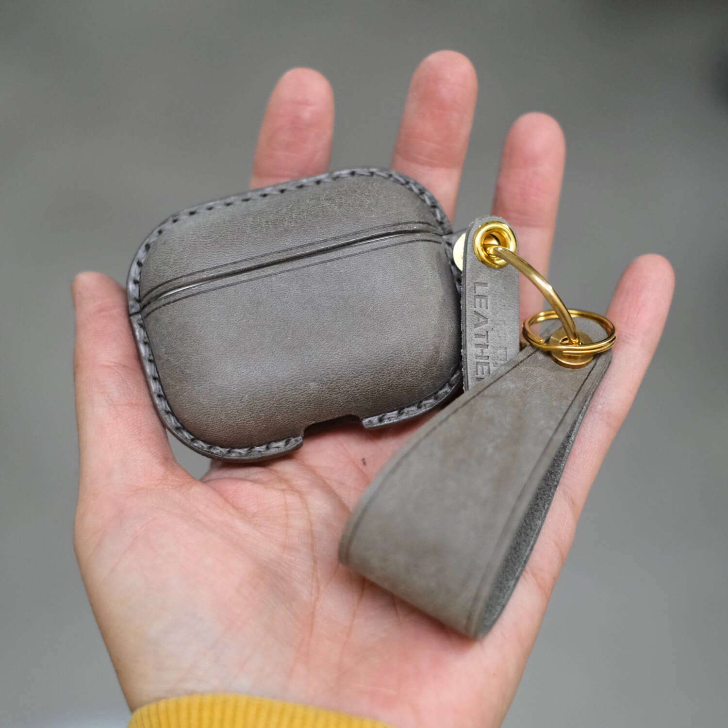 Elephant grey handcrafted personalized leather earbuds case for AirPods Pro 3 with keychain and leather strap held in hand - Integrated design