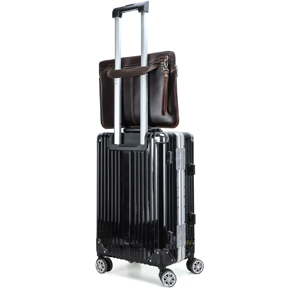 使用シーン - レザー製ノートパソコンスリーブはトロリーストラップでスーツケースの取っ手に固定され、黒のハードシェルスーツケースの上に置かれている。