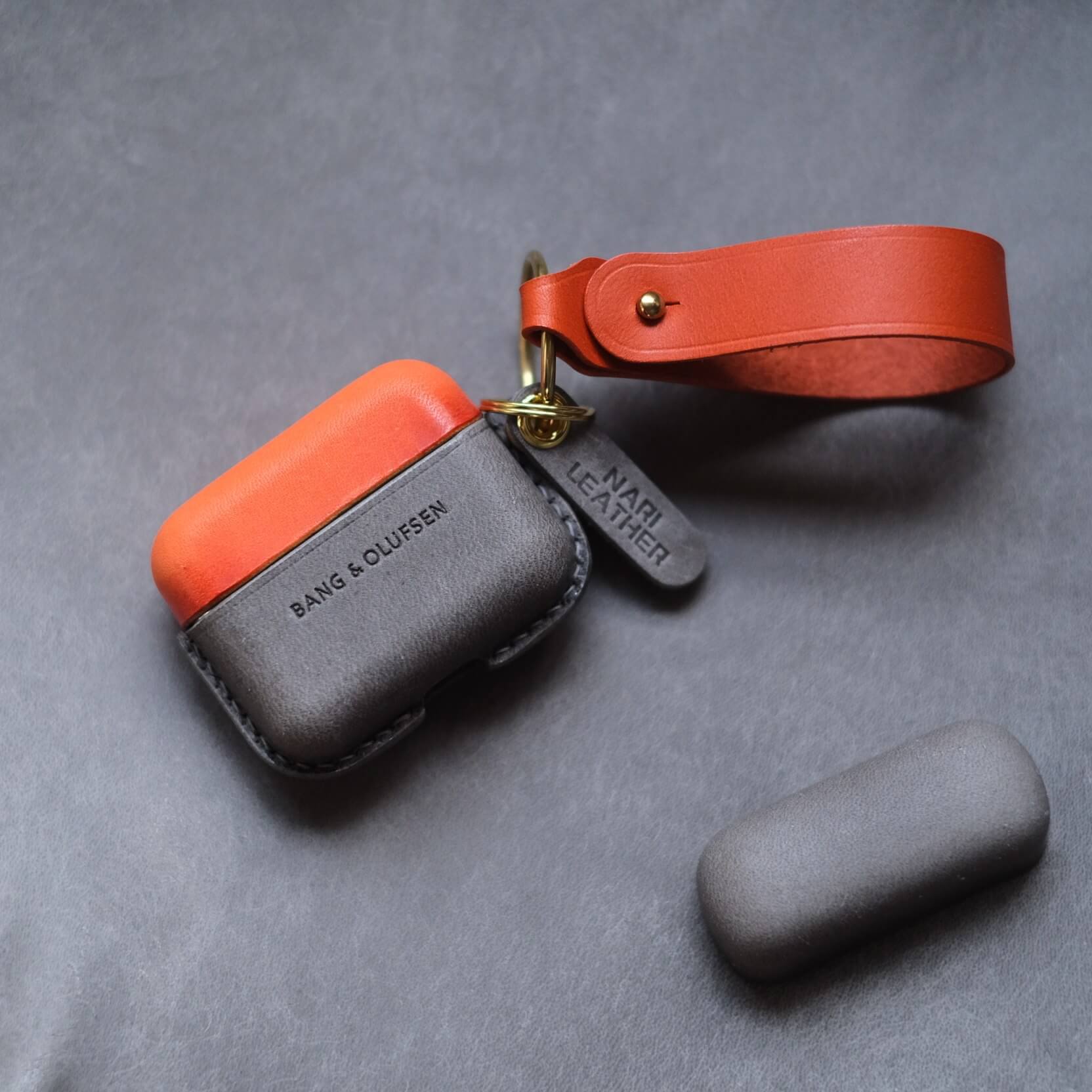 Étui pour écouteurs Bang & Olufsen Beo Grace en cuir orange et gris éléphant, personnalisé et fabriqué à la main, avec porte-clés latéral et lanière en cuir orange.