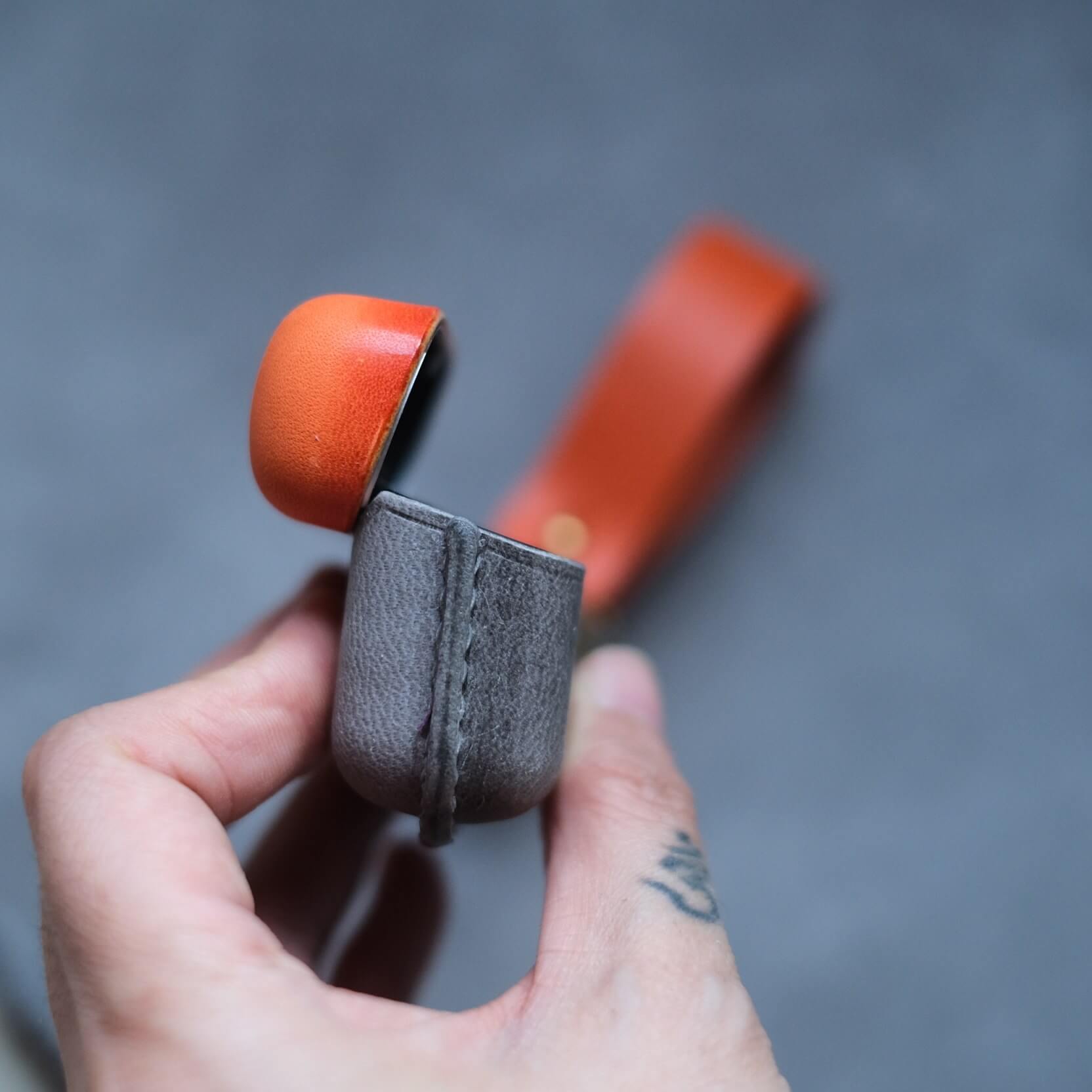 Étui pour écouteurs Bang & Olufsen Beo Grace en cuir orange et gris éléphant, personnalisé et fabriqué à la main, avec porte-clés latéral et lanière en cuir orange - gros plan sur les coutures latérales et le couvercle ouvrant.