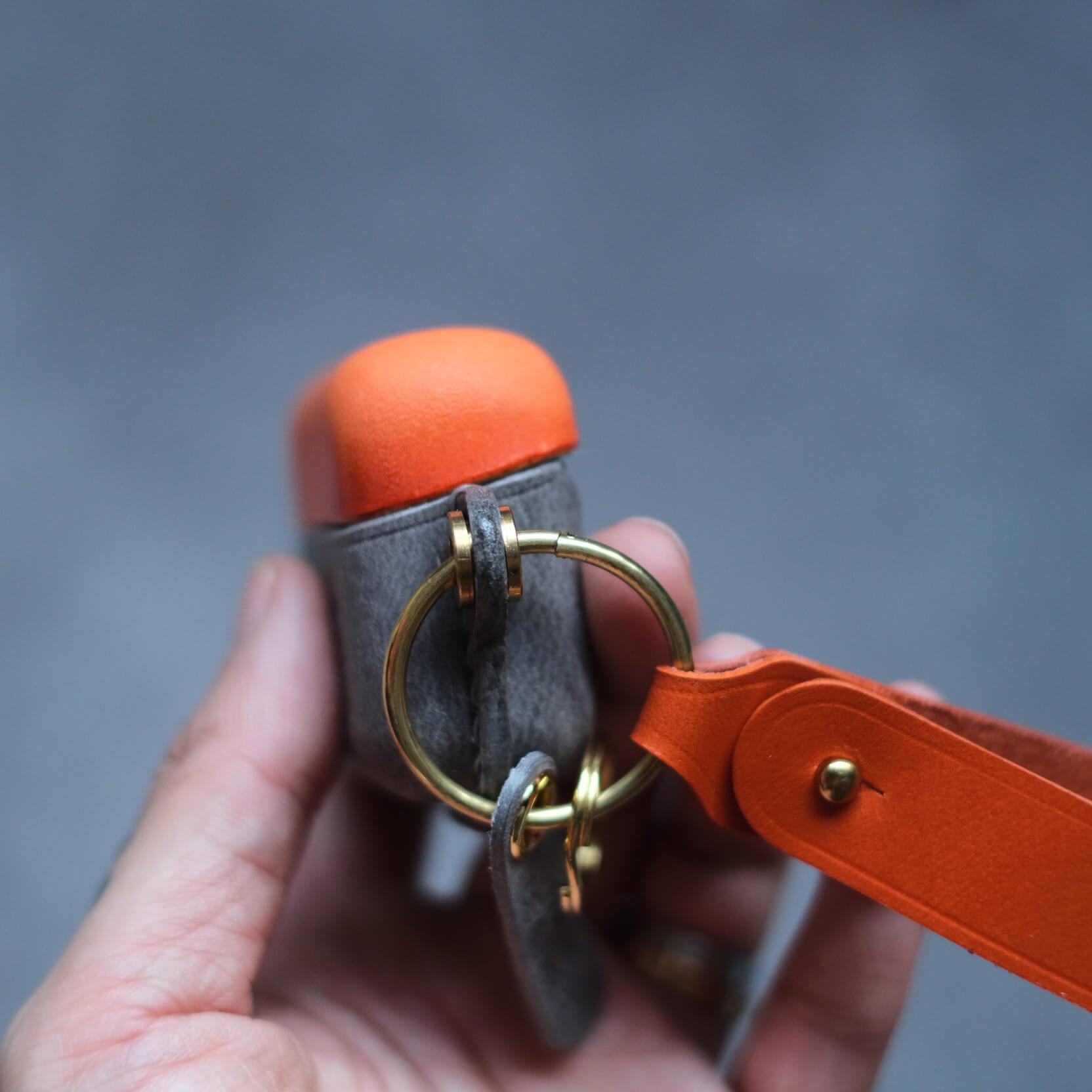 Étui pour écouteurs Bang & Olufsen Beo Grace en cuir orange et gris éléphant, fabriqué à la main et personnalisé - gros plan sur le porte-clés latéral et la lanière en cuir orange