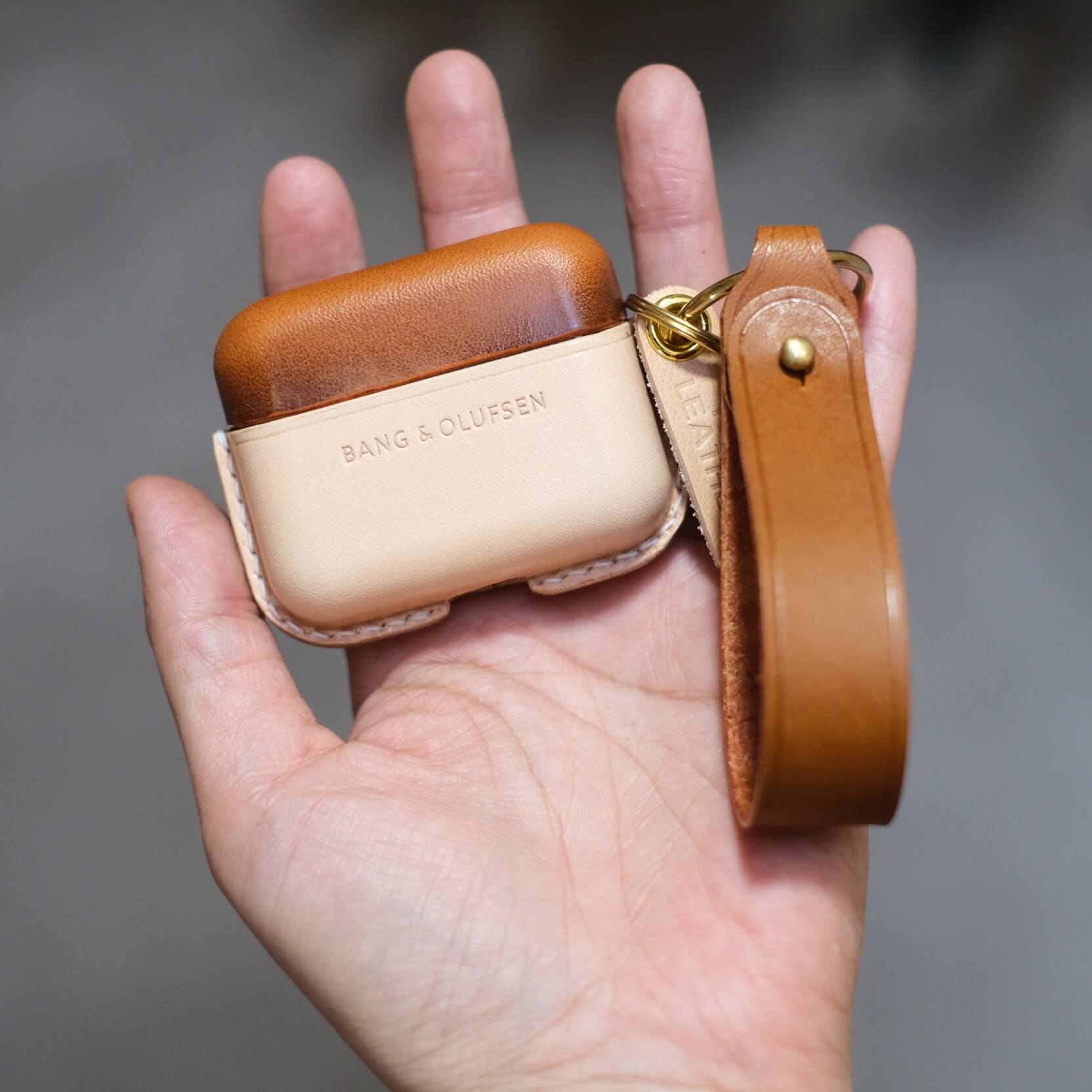 Étui pour écouteurs Bang & Olufsen Beo Grace en cuir marron et beige assorti, personnalisé et fabriqué à la main, avec porte-clés latéral et lanière en cuir orange.