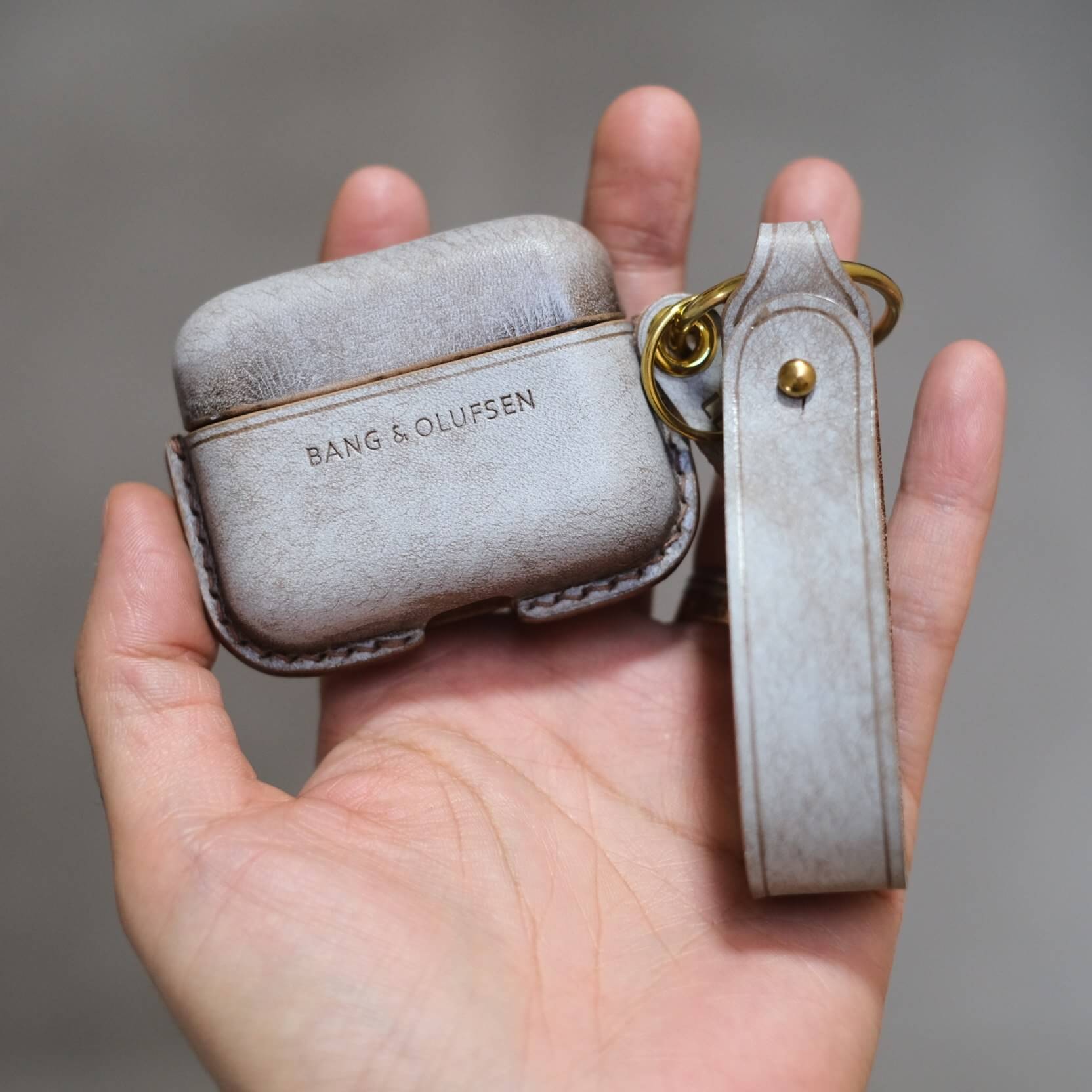 Étui pour écouteurs Bang & Olufsen Beo Grace en cuir marron clair mat personnalisé et fabriqué à la main, style cire brumeuse, avec porte-clés latéral et lanière en cuir orange.