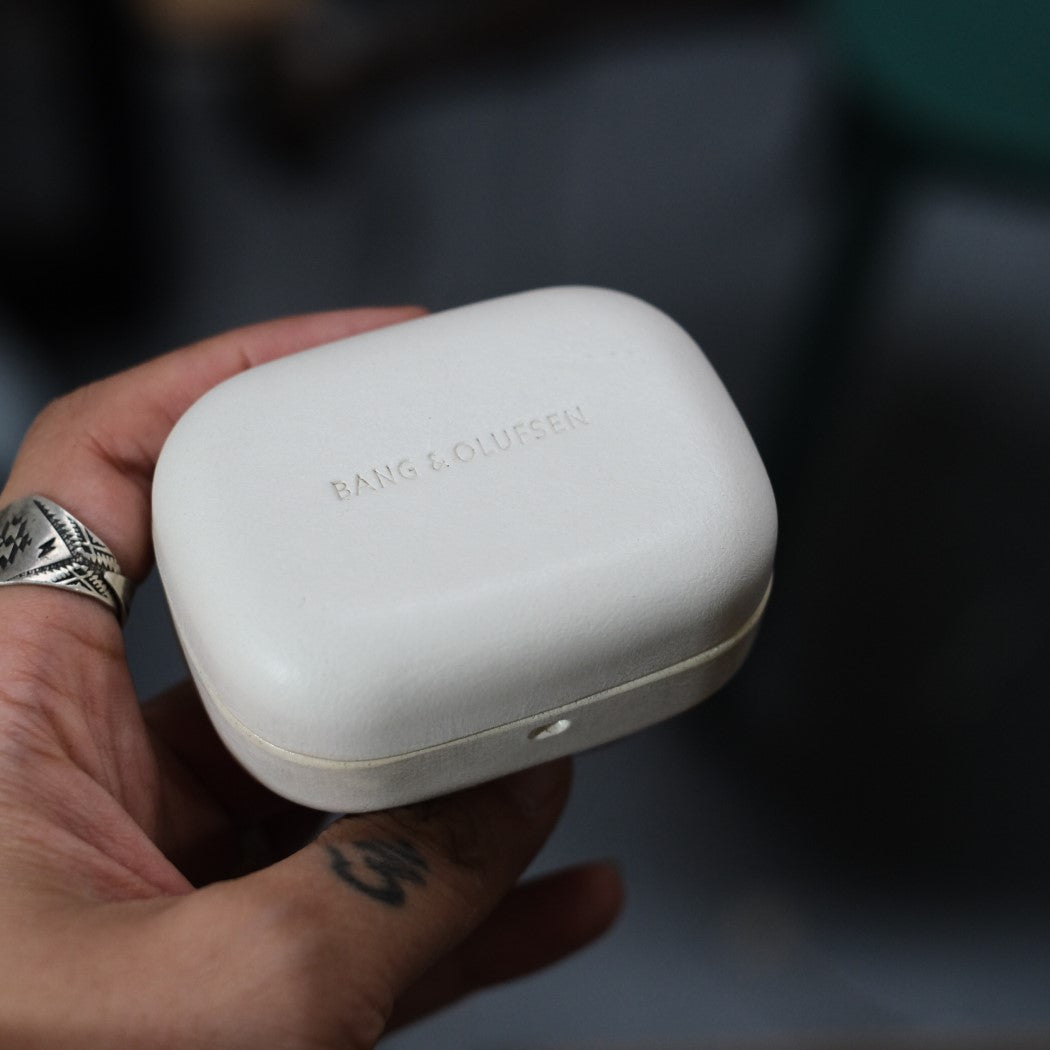 Close-up hand holding a white genuine leather earbud case engraving &quot;Bang &amp; Olufsen&quot; designed for Bang &amp; Olufsen Beoplay EX and Eleven