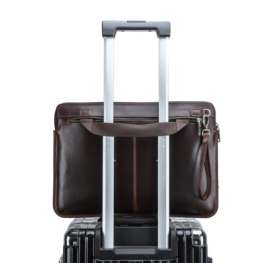 ビジネスや旅行用に、スーツケースのハンドルに固定できるキャリーストラップ付きレザー製ノートパソコンスリーブ。黒いハードシェルスーツケースの上に置かれています。