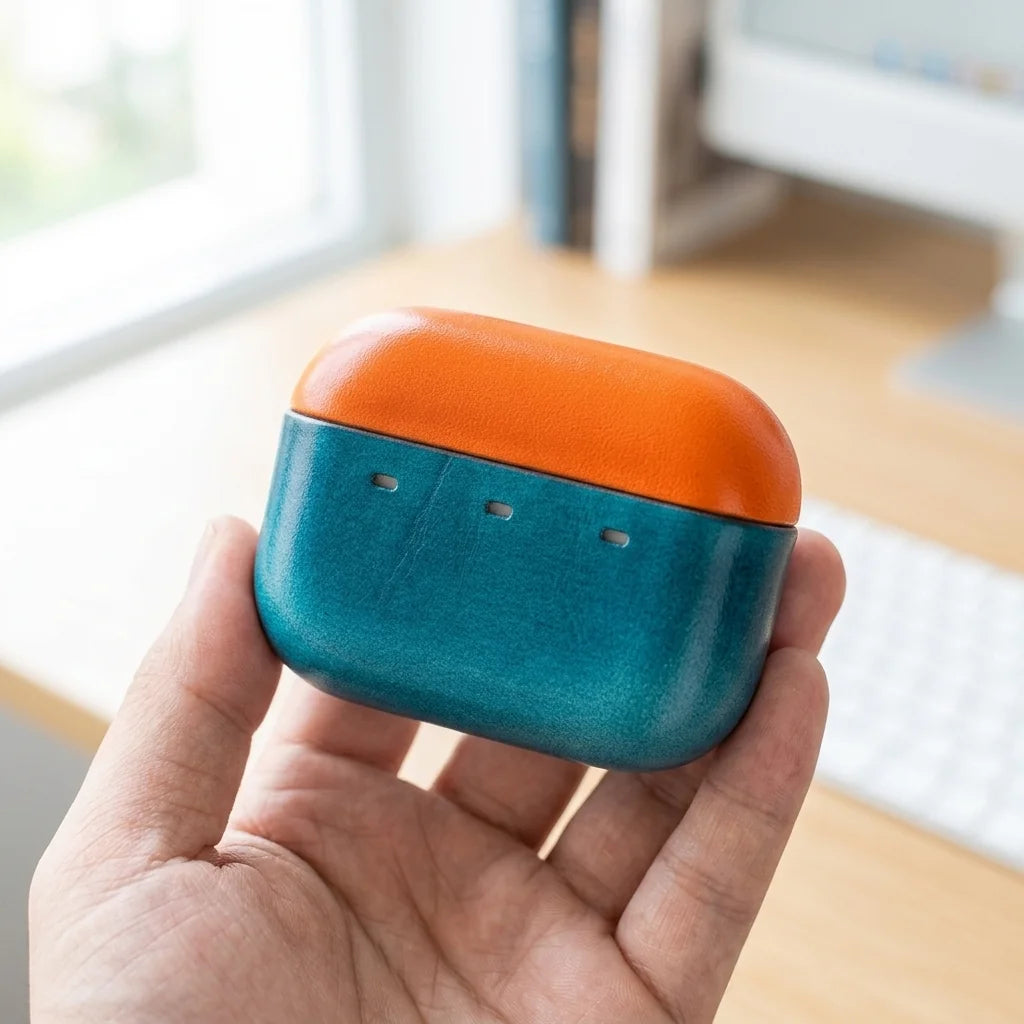 Master & Dynamic MW09 leather case, orange and teal two-tone design, front view showing LED status cutouts