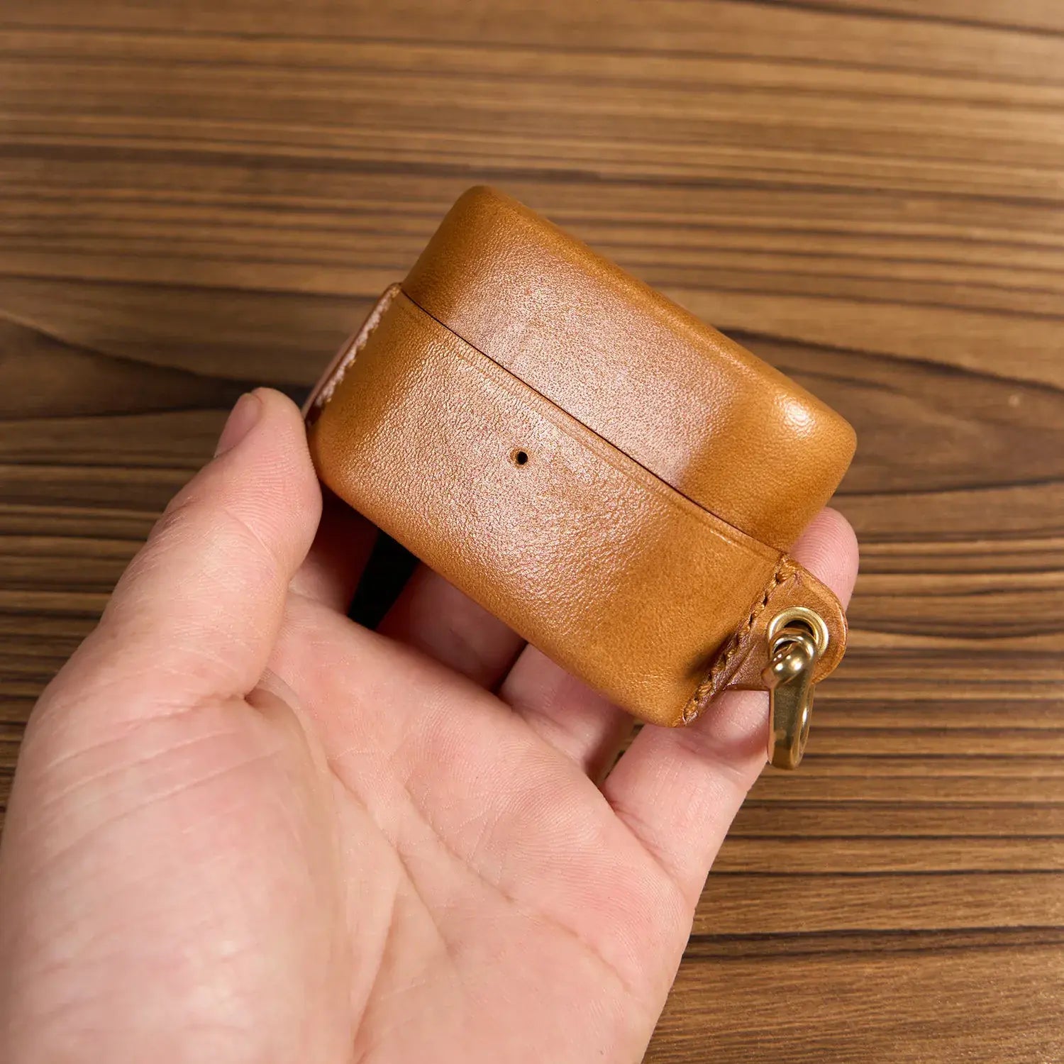 Una mano che tiene la custodia chiusa in pelle marrone per Sony WF-1000XM6 su sfondo in legno, design compatto e portatile.