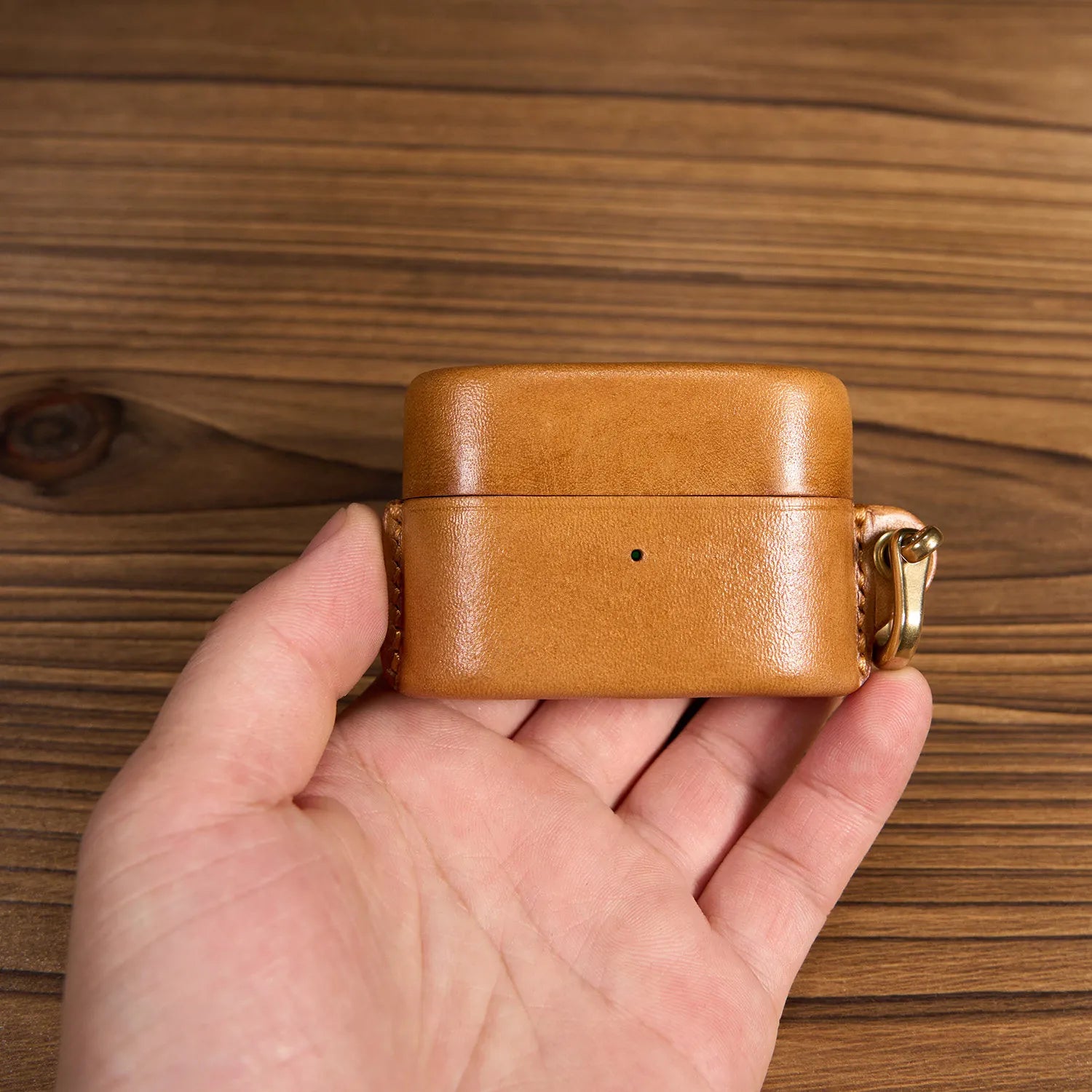 Handcrafted tan leather case for Sony WF-1000XM6 earbuds held in hand, showcasing premium pebble grain texture and vintage brass hook.